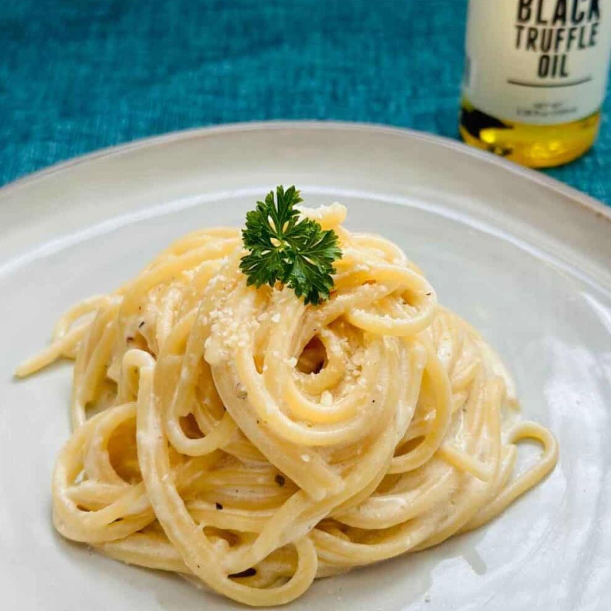 Creamy truffle pasta with black truffle oil and Parmesan, garnished with fresh parsley on a white plate.