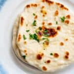 A stack of freshly baked and golden-brown, soft and fluffy naan breads with characteristic char marks.
