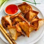 Golden brown crispy crab rangoon, filled with savory crabmeat and cream cheese, served alongside a side of tangy sweet and sour sauce, offering a delightful appetizer bursting with flavor and texture.