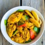 Succulent chicken pieces simmered in a vibrant yellow turmeric sauce, accompanied by colorful bell peppers and potatoes, creating a visually stunning and flavorful dish.