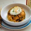 Plated savory fried rice mixed with ground beef and tangy kimchi, adorned with a perfectly cooked egg on top, creating a mouthwatering Korean-inspired dish.