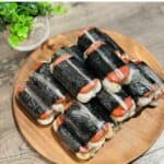 A stack of Spam musubi wrapped in plastic film: Layers of grilled Spam, sticky rice, and nori seaweed, a popular Hawaiian snack, neatly packaged and ready to enjoy.