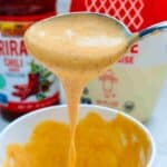 A creamy and spicy condiment blending the flavors of sriracha chili sauce and mayonnaise being drizzled from a spoon into a bowl.