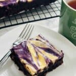 Slice of a decadent fusion of rich chocolate brownie swirled with vibrant ube and creamy cheesecake layers of ube cheesecake marble brownie.
