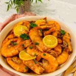 Plump shrimp nestled in a deep plate, bathed in a luscious spicy garlic butter sauce, offering a tantalizing blend of flavors and aromas.