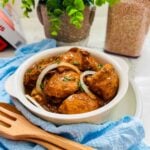Chicken bistek braised in soy sauce and calamansi on a white bowl with fresh onion rings on top, blue napkins and wooden spoon and pork on the side.