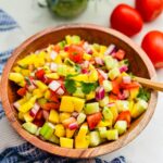 Salsa de mango on a wooden bowl with wooden spoon and a tblue and white table cloth on the side.
