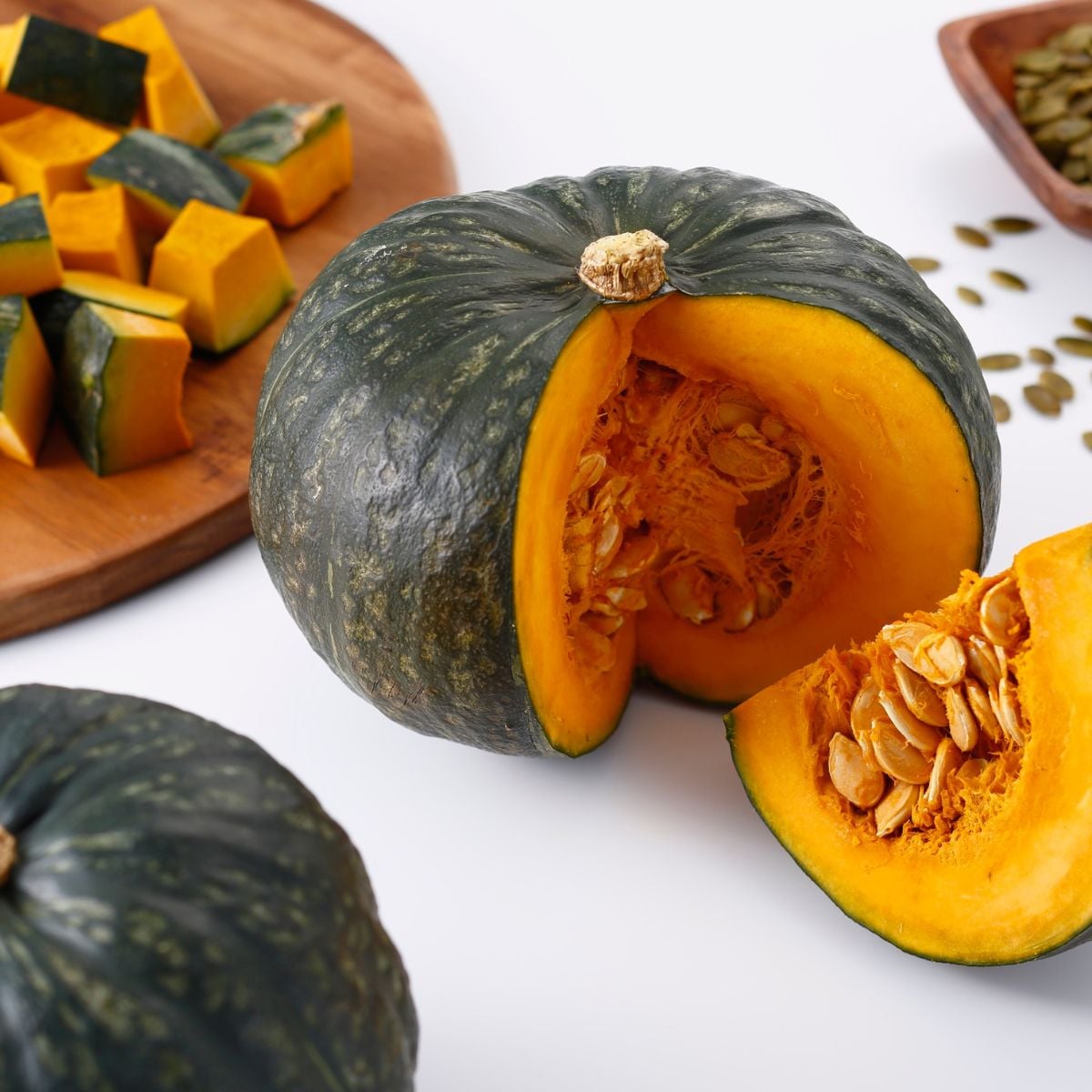 Whole and cut kabocha squash showing bright orange flesh and seeds, with cubed squash on a wooden cutting board.