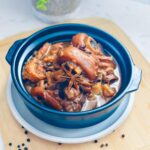 Pork humba in a claypot with plate and wooden board underneath.