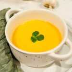Golden Kabocha Squash Soup served in a white bowl, showcasing its vibrant color and creamy texture.