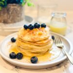 A mouthwatering stack of Maja Blanca pancakes topped with blonde butter syrup and fresh blueberries.