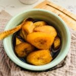 Sliced Minatamis na saging cooked in brown sugar syrup served in a light green round bowl with a wooden spoon.