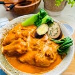 Oxtail karekare with creamy orange peanut sauce with snake beans, eggplant and bokchoy in a rustic bowl.