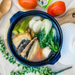 A savory Filipino soup with bangus fish simmered in a sour tamarind broth, served in a black clay pot.