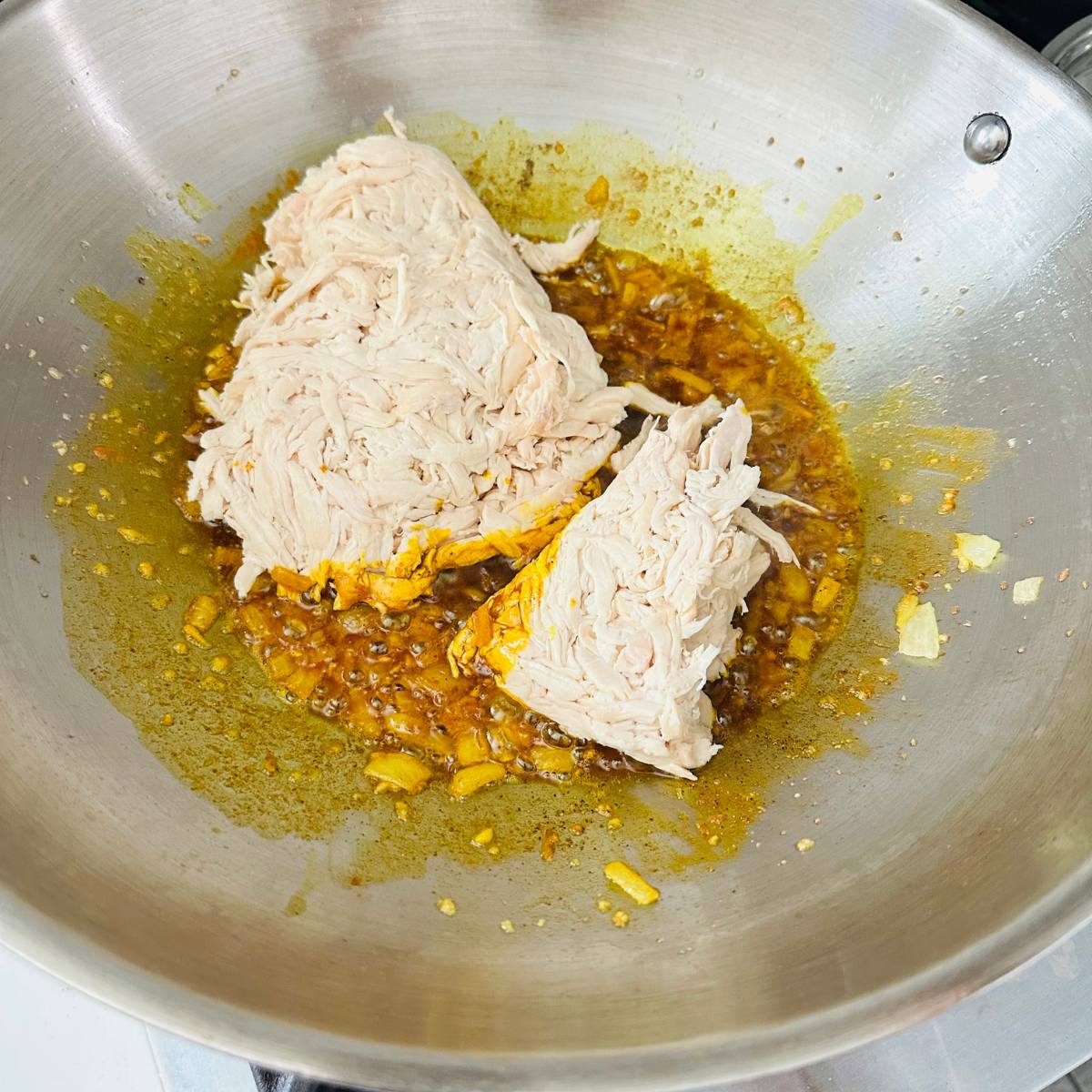 Shredded rotisserie chicken added to the pan with aromatics.