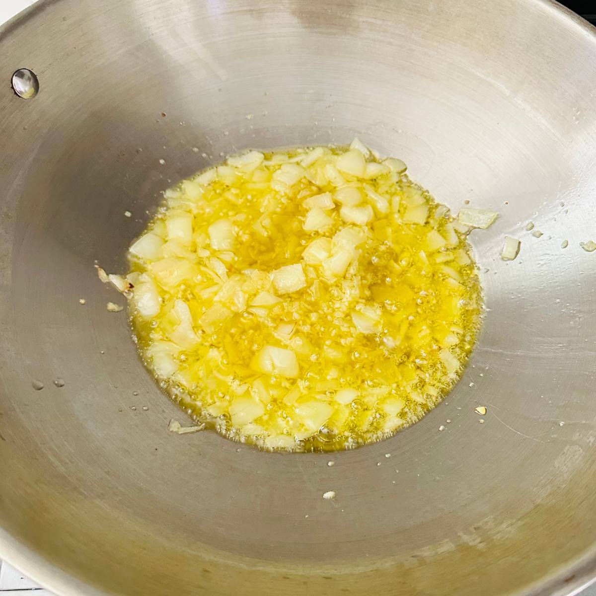 Garlic and sliced onions sautรฉing in oil in a pan.