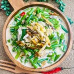 Wooden bowl filled with aromatic gising gising featuring tender green beans, smoked tinapang bangus flakes, and creamy coconut milk, a traditional Filipino delicacy