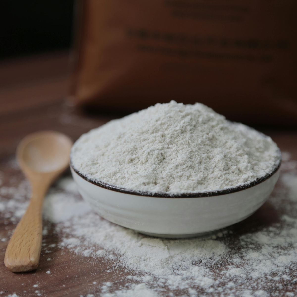Bowl of rice flour with a wooden spoon on a floured wooden surface.