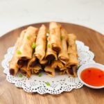 A wooden plate piled with Crab Rangoon egg rolls, golden-brown and crispy, ready to be served.
