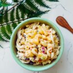 Macaroni salad in a bowl, showcasing cooked pasta mixed with mayonnaise, carrots, pineapples, pickle relish, onions, salt, and pepper, ready to be served and enjoyed.