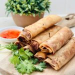 A close-up of a pile of golden-brown Chicken Lumpiang Shanghai, Filipino spring rolls, neatly arranged on a plate.