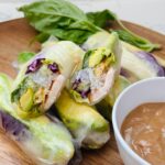 Close-up of Shrimp and Avocado Spring Rolls with Thai Peanut Sauce on a plate. The fresh spring rolls are filled with shrimp, avocado, and vegetables, and are served alongside a bowl of creamy Thai peanut sauce for dipping.