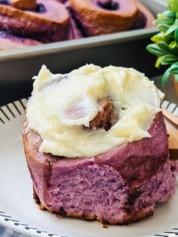 Close-up of Ube cinnamon Rolls topped with cream cheese frosting. The rolls are glazed with a smooth, creamy frosting that complements the vibrant purple ube dough, creating a decadent and visually appealing dessert.