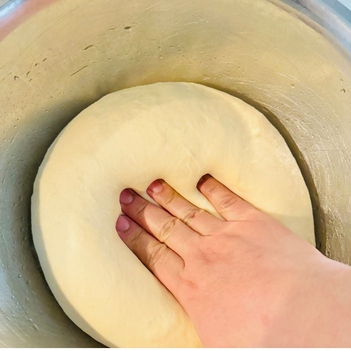 Pressing dough to release gas.