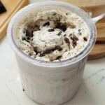 A pint container of freshly spun vanilla ice cream with chocolate chips added as mixins, showing a rich, creamy texture.