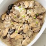 Tender slices of beef lengua served in a rich, creamy garlic butter sauce, garnished with fresh herbs on a white serving dish.