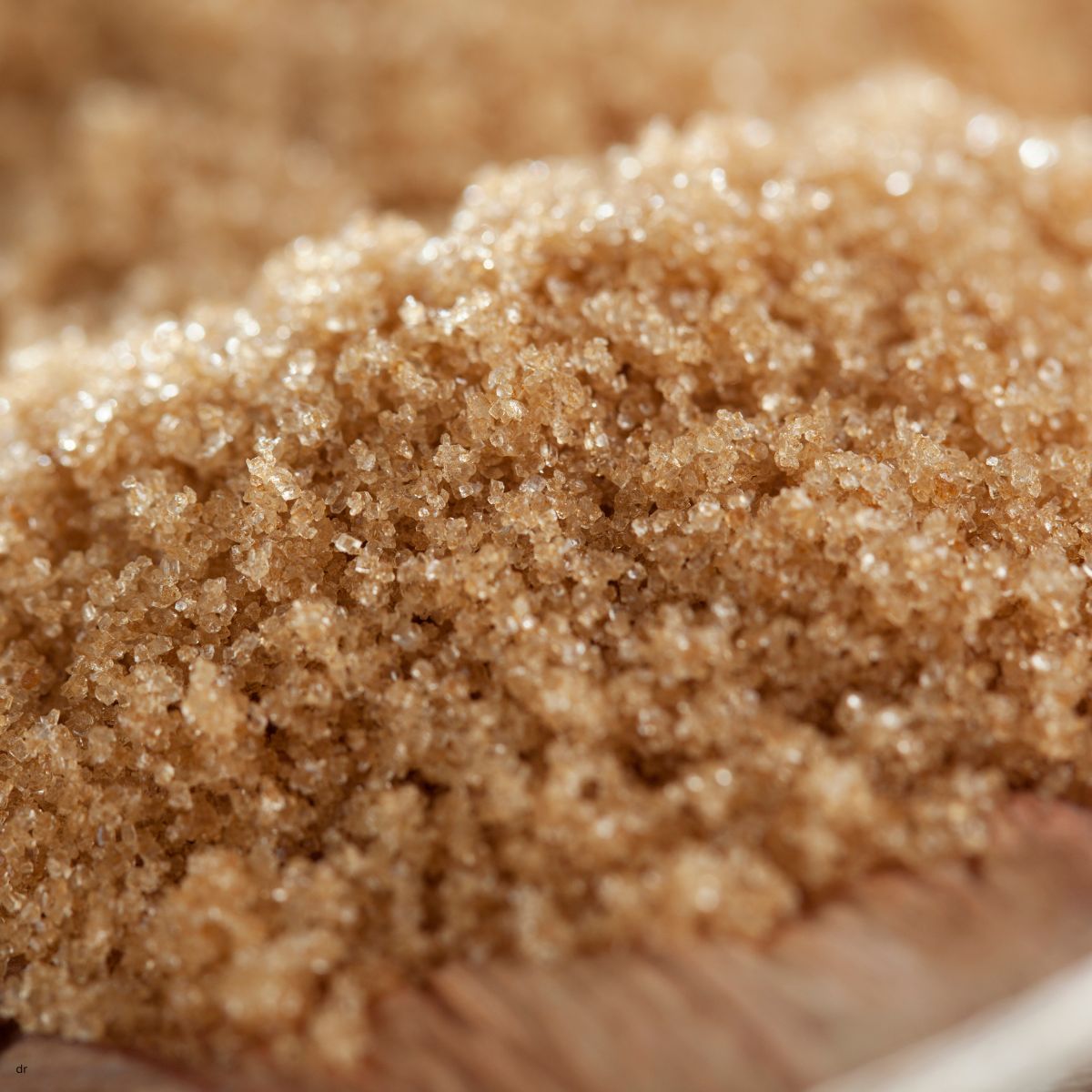 Close-up of brown sugar crystals piled on a wooden spoon.