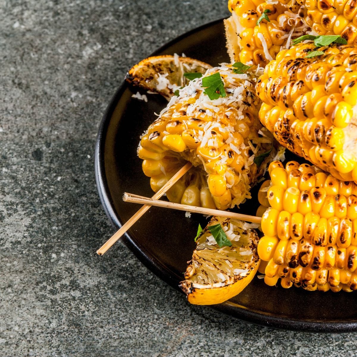 Grilled corn on the cob with charred kernels, grated cheese, fresh herbs, and grilled lime wedges.