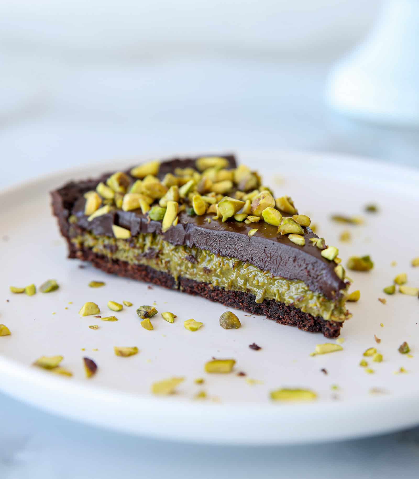 Close-up of a decadent slice of rich chocolate tart topped with chopped pistachios and a glossy chocolate glaze, inspired by Dubai flavors.