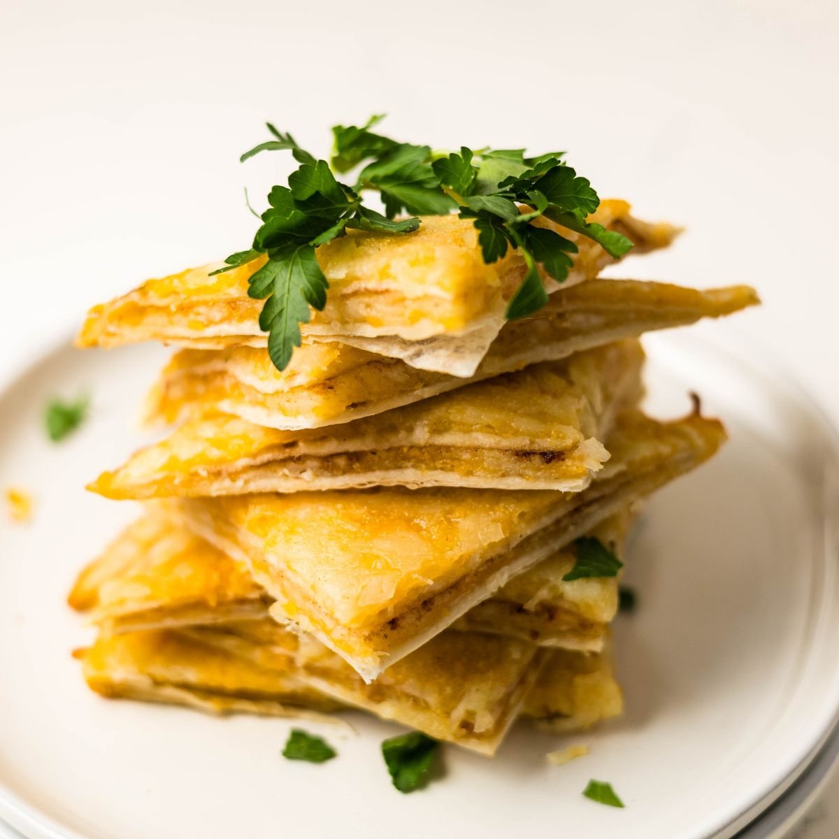 Slices of air fryer cheesy tortilla garlic bread stacked on a plate, showing crispy edges and melted cheese.