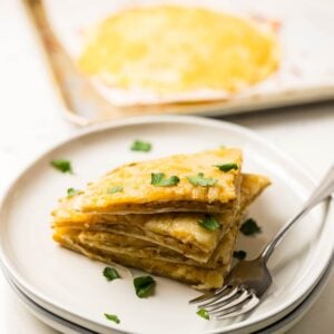 Slices of air fryer cheesy tortilla garlic bread stacked on a plate, showing crispy edges and melted cheese.