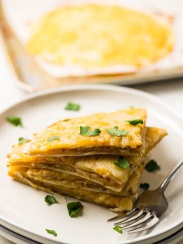 Slices of air fryer cheesy tortilla garlic bread stacked on a plate, showing crispy edges and melted cheese.