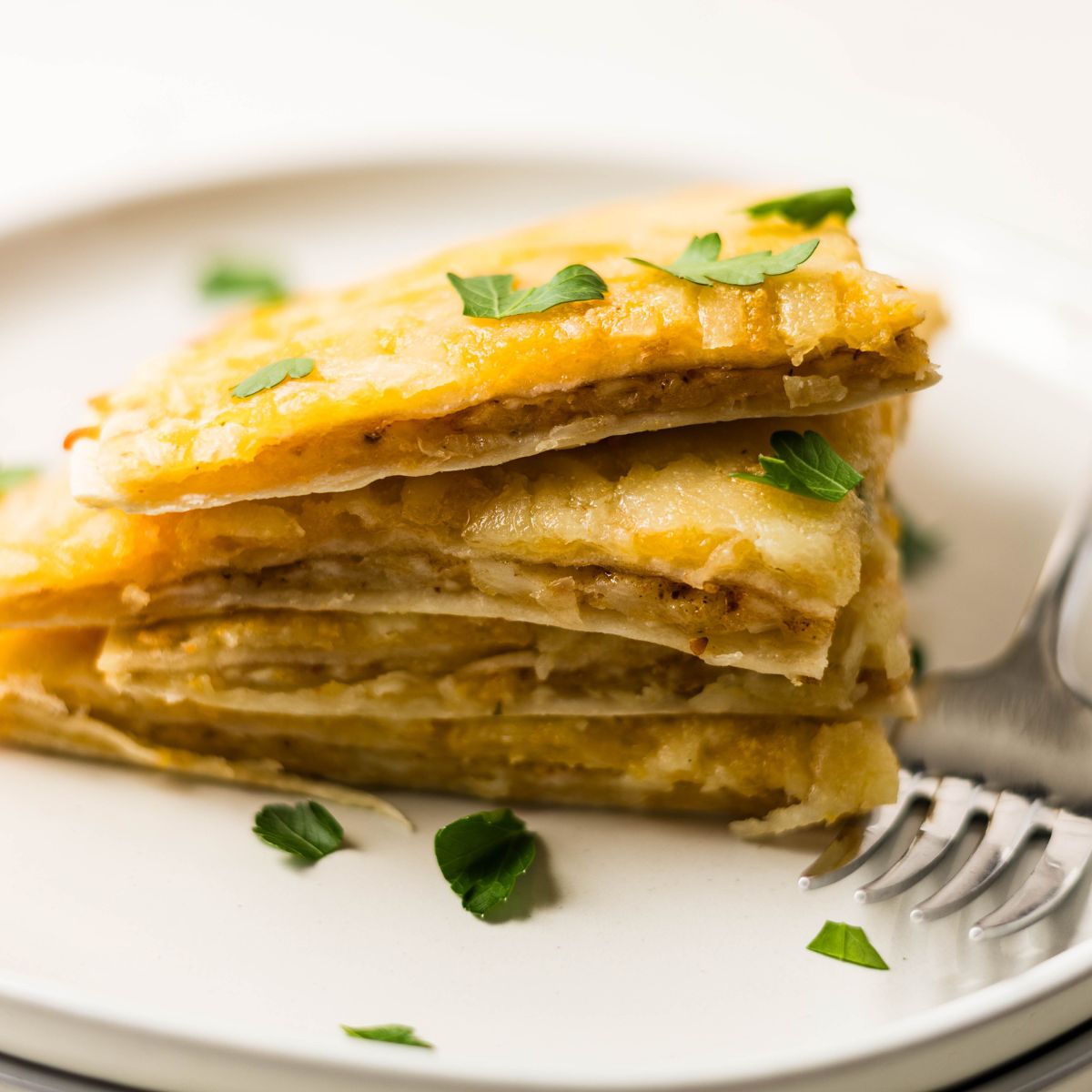 Slices of air fryer cheesy tortilla garlic bread stacked on a plate, showing crispy edges and melted cheese.