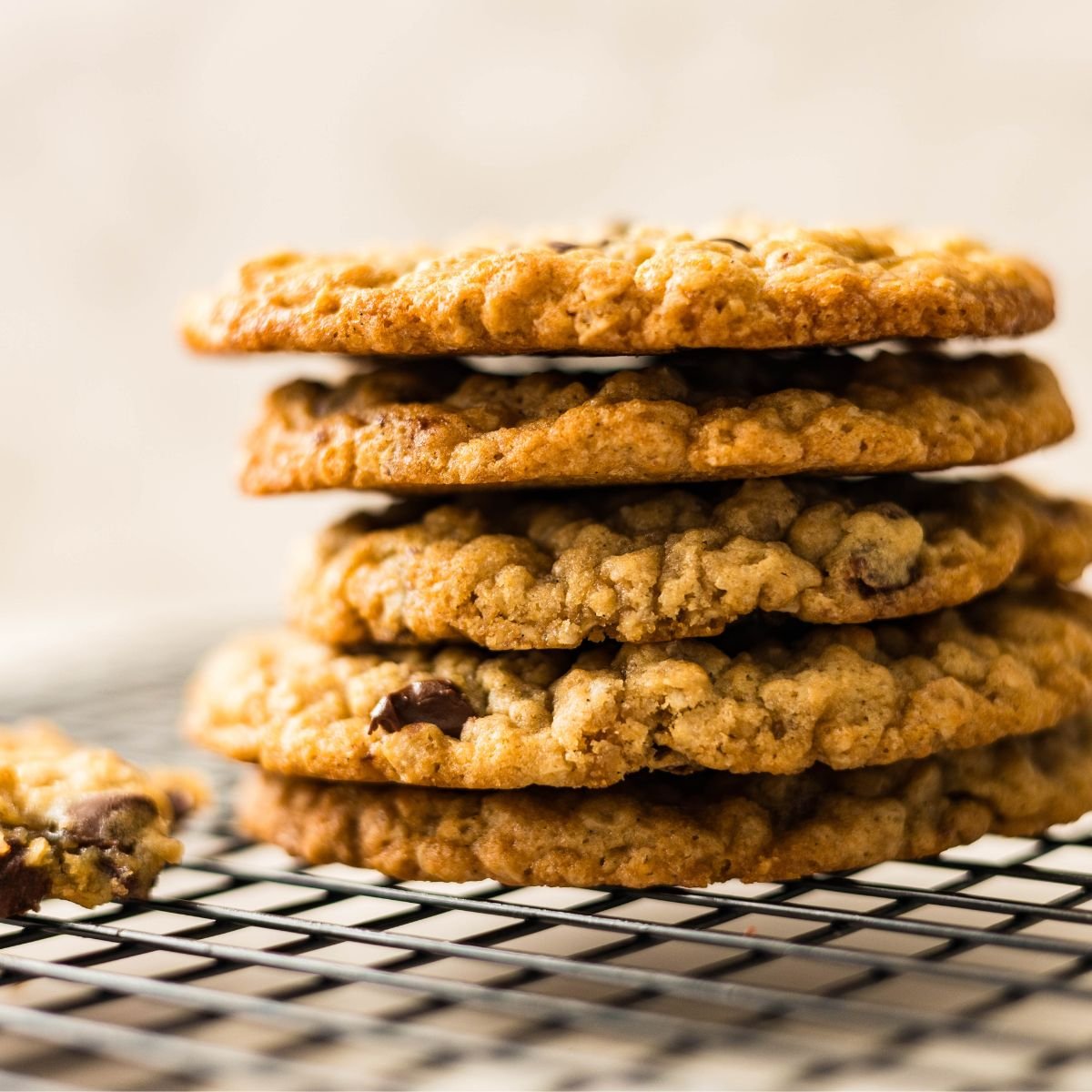 Brown butter oatmeal chocolate chip cookies stacked on a cooling rack with melted chocolate and golden edges.