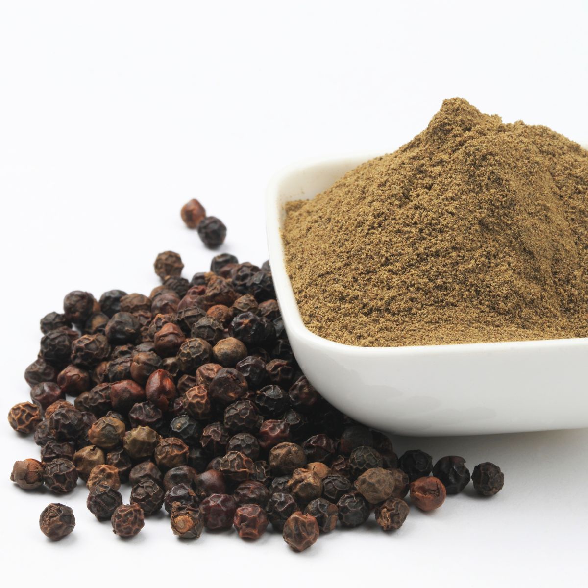 Ground black pepper in a white bowl surrounded by whole black peppercorns.