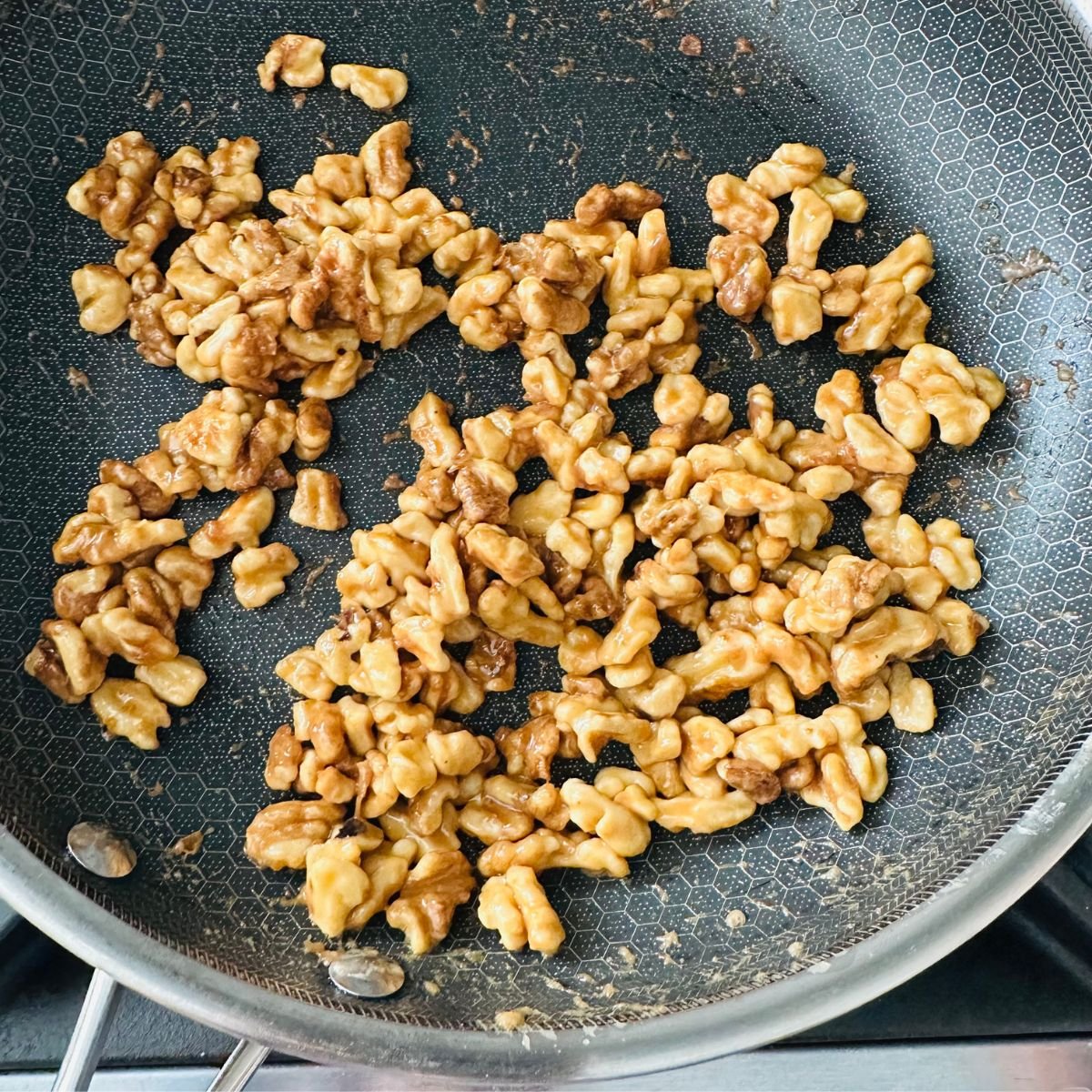 Cooking walnuts on the stovetop while stirring so maple syrup caramelizes evenly.