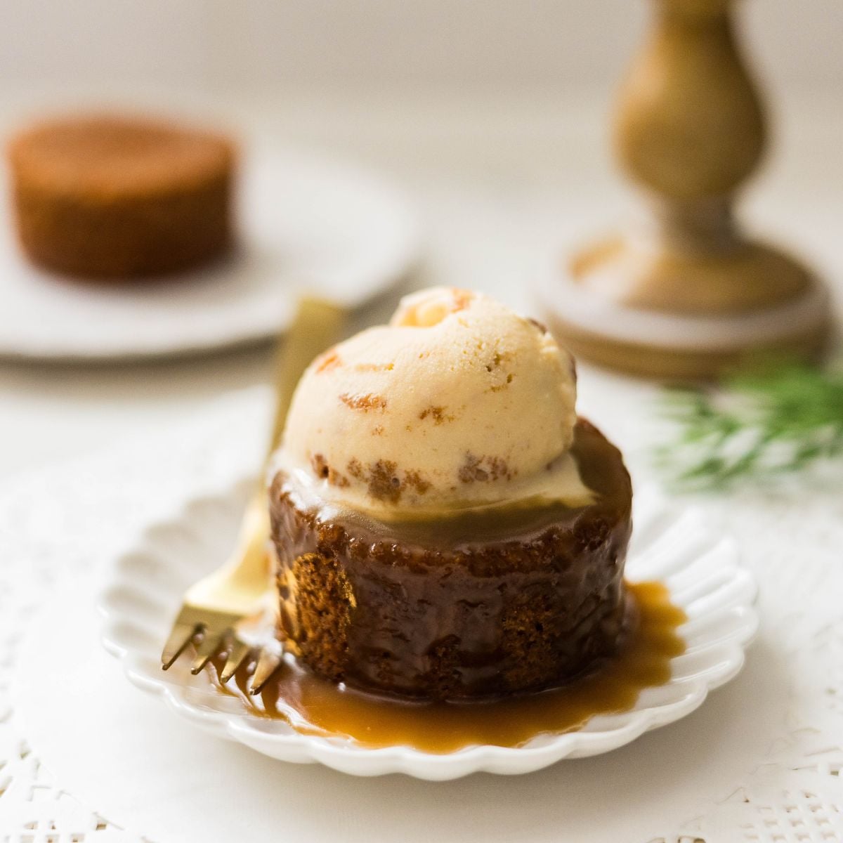 Sticky date pudding topped with ice cream on a white plate.