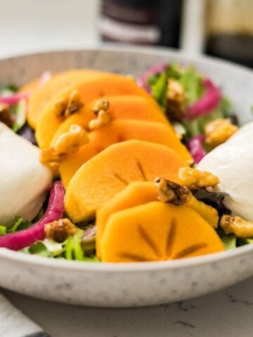 A cozy fall salad featuring spring mix, burrata, and ripe persimmon — a bright, creamy, and fresh seasonal dish.