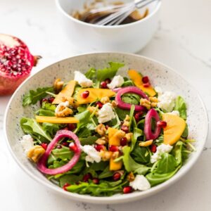 Easy arugula and pomegranate salad with goat cheese, candied walnuts, and balsamic dressing — simple fall salad recipe.