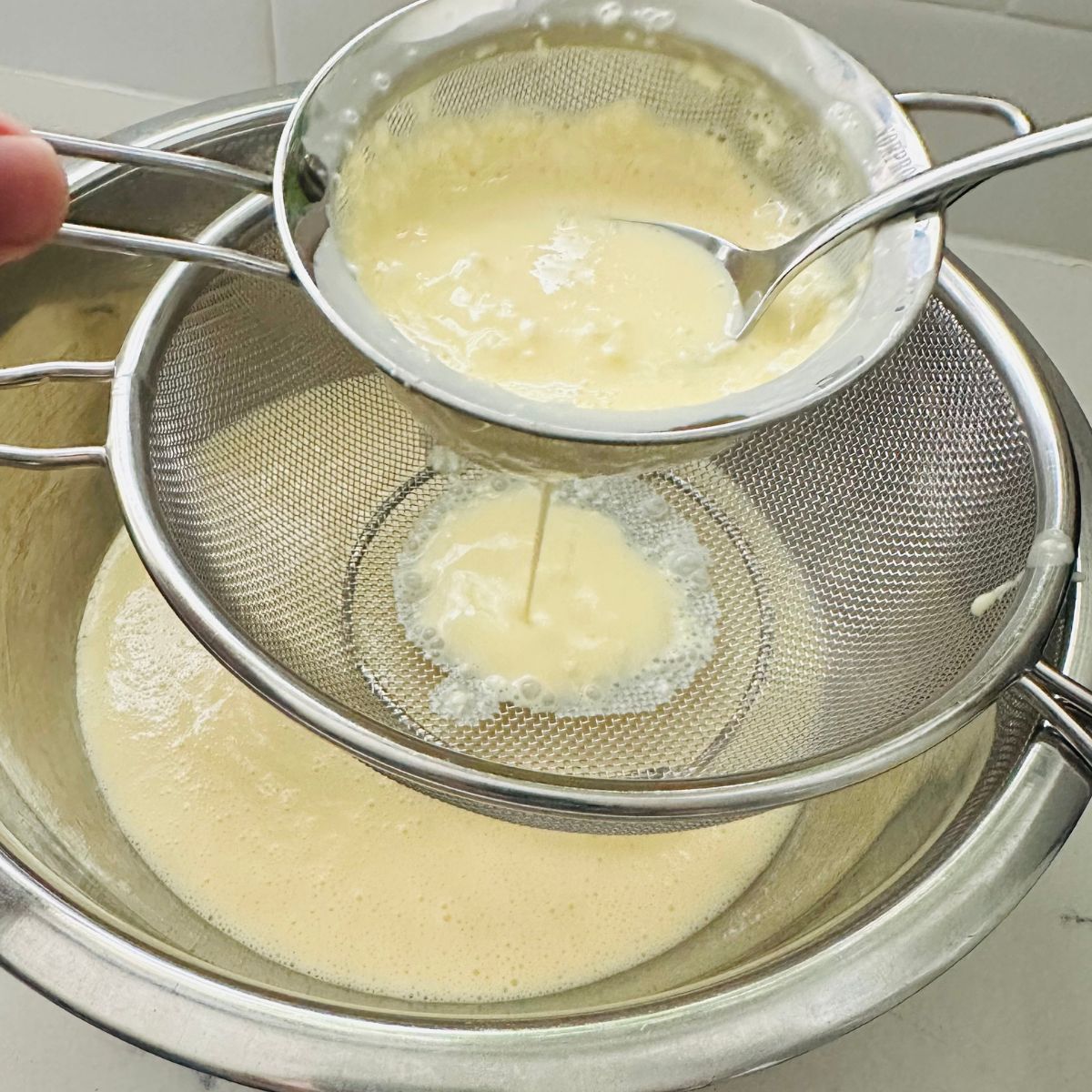 Straining creamy eggnog mixture to remove lumps before baking.