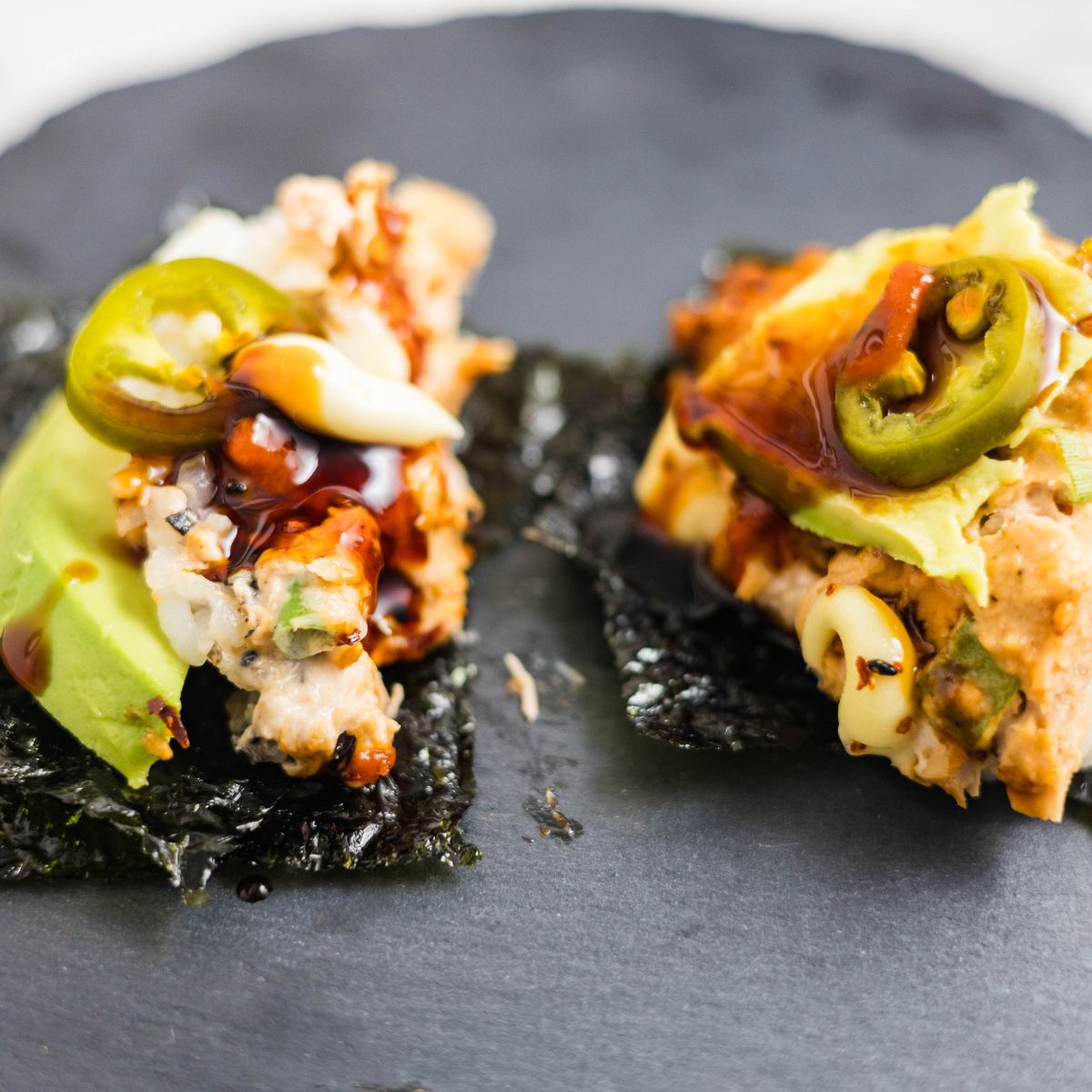 Spoonful of spicy tuna sushi bake served on seaweed with avocado and drizzled with eel sauce, sriracha, and mayo.