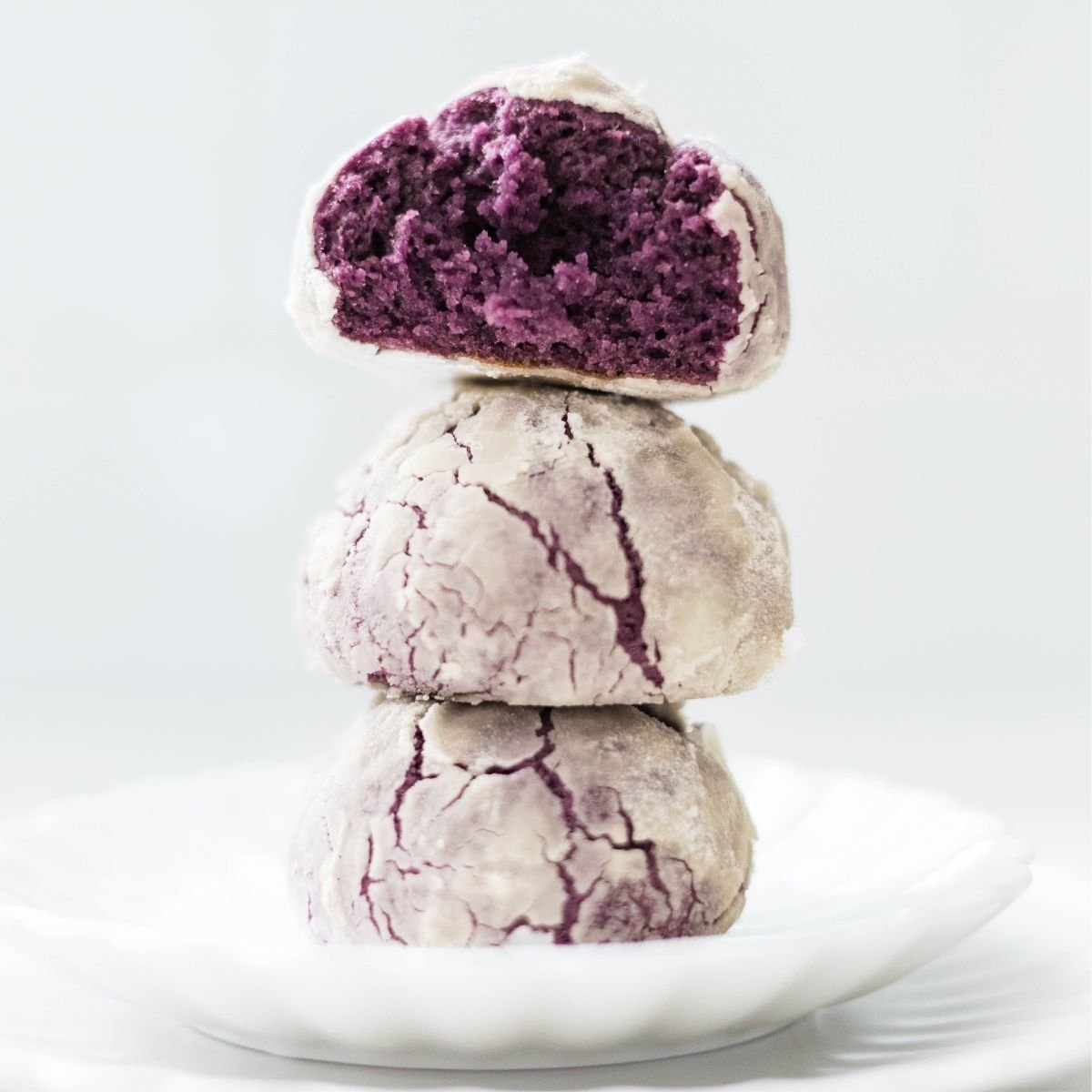Freshly baked ube crinkle cookies stacked, showing soft moist purple center and crackled tops.