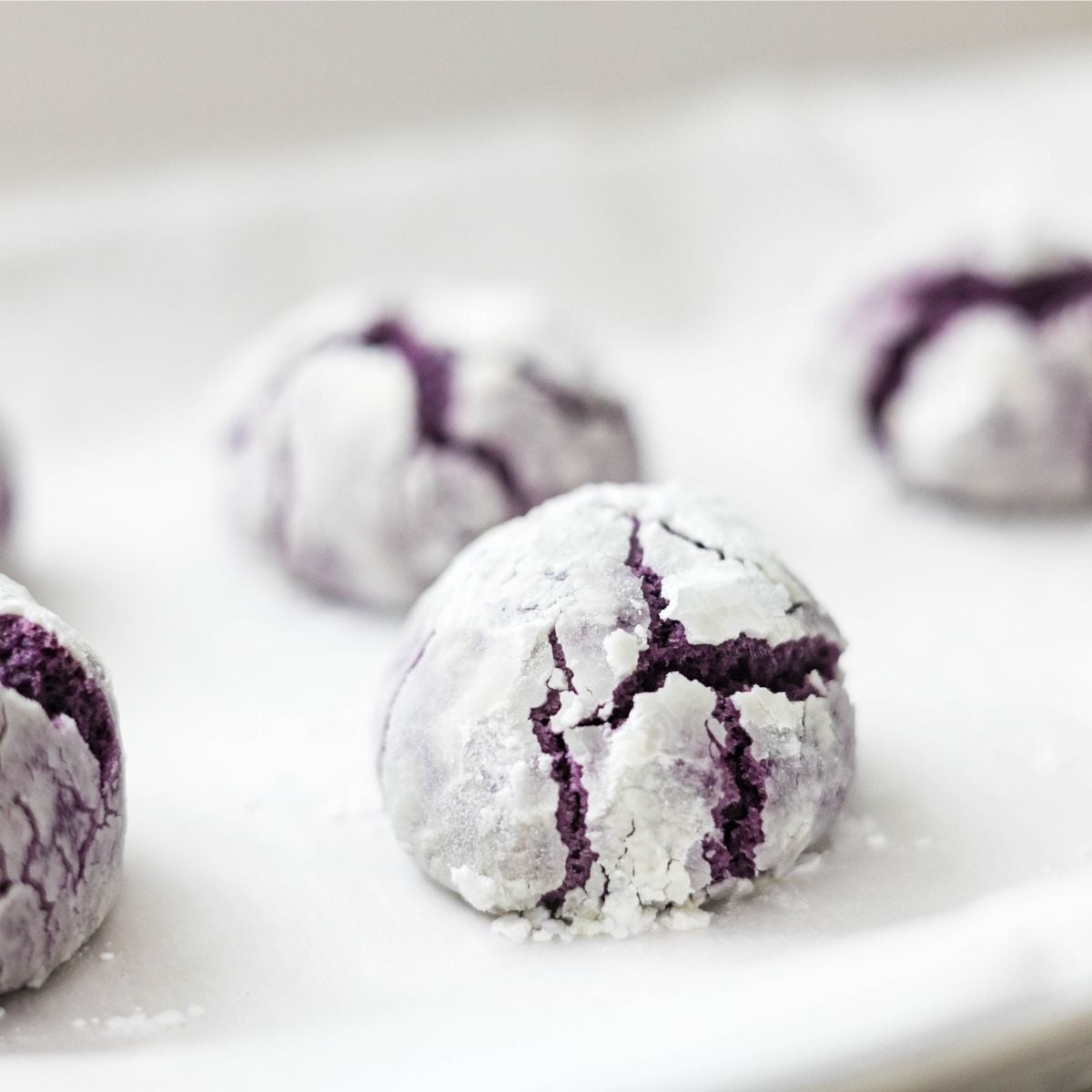 Freshly baked ube crinkle cookies cooling on a wire rack with crisp, cracked tops.