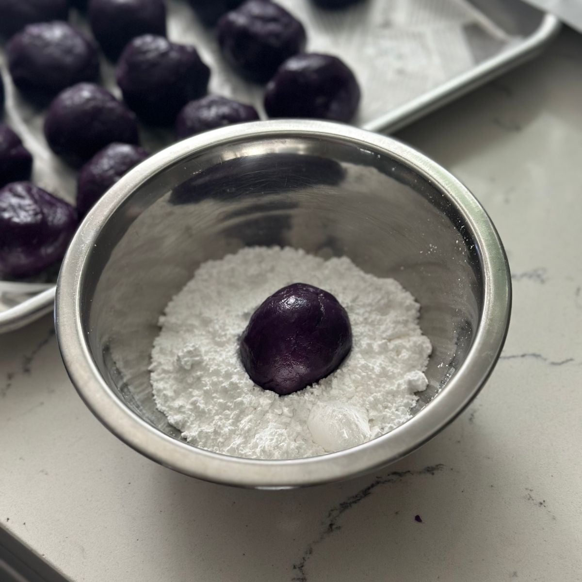Rolling ube cookie dough balls in powdered sugar for classic crinkle effect