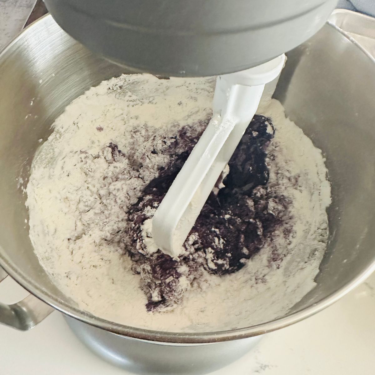 Blending dry ingredients into ube cookie batter with a mixer until smooth and purple