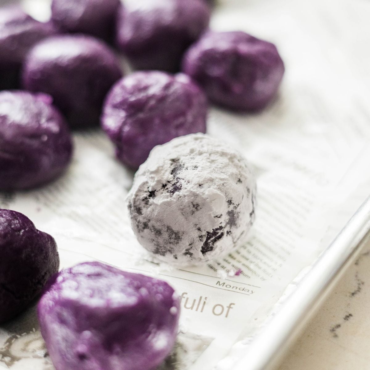 Rolling ube cookie dough balls in powdered sugar for classic crinkle effect